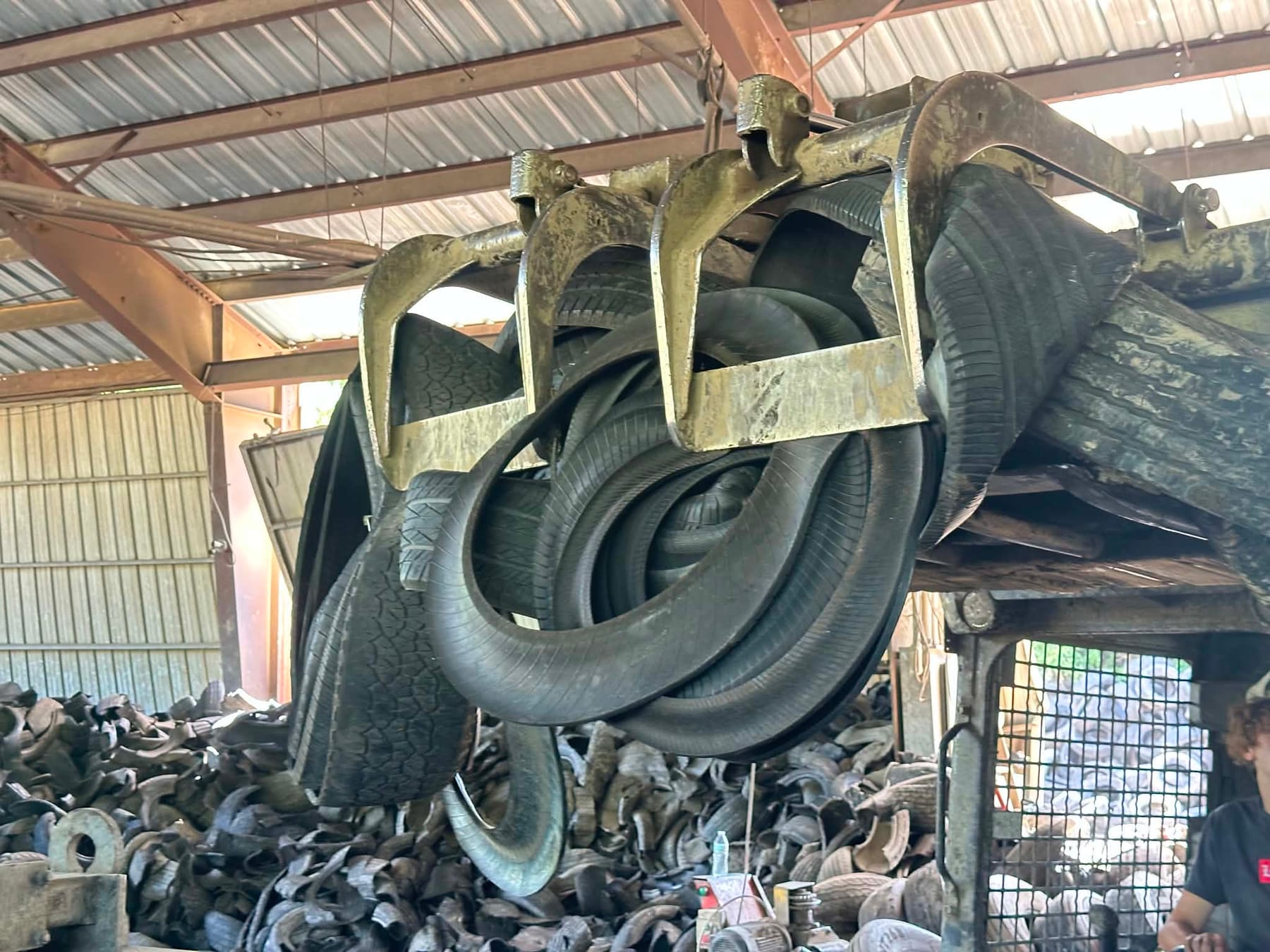 A grapple lifting a load of scrap tires above the pile inside the Penn Turf processing shed